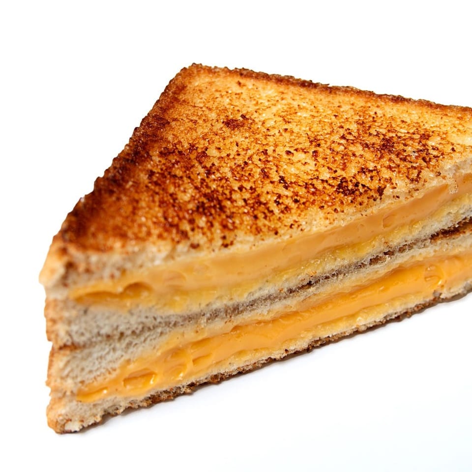 Triangular toasted grilled cheese sandwich with melted cheddar layers on a white background.